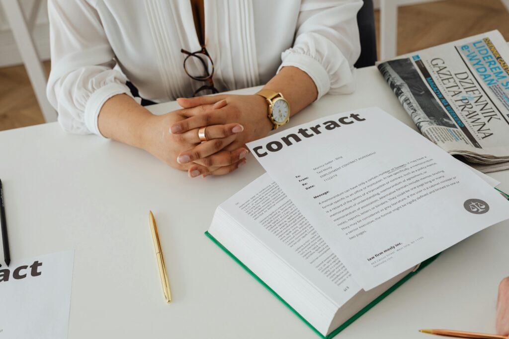 Businesswoman sitting at desk reviewing contract with legal documents and newspaper.